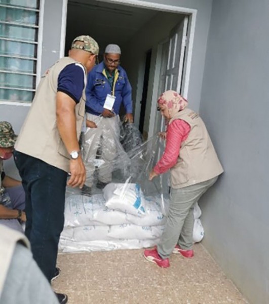 Three people demonstrate how to stack and use sandbags for flood protection in the doorway of a home